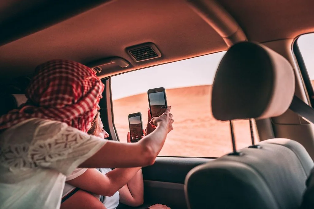 Tourists taking photos from inside a car in the Dubai desert landscape