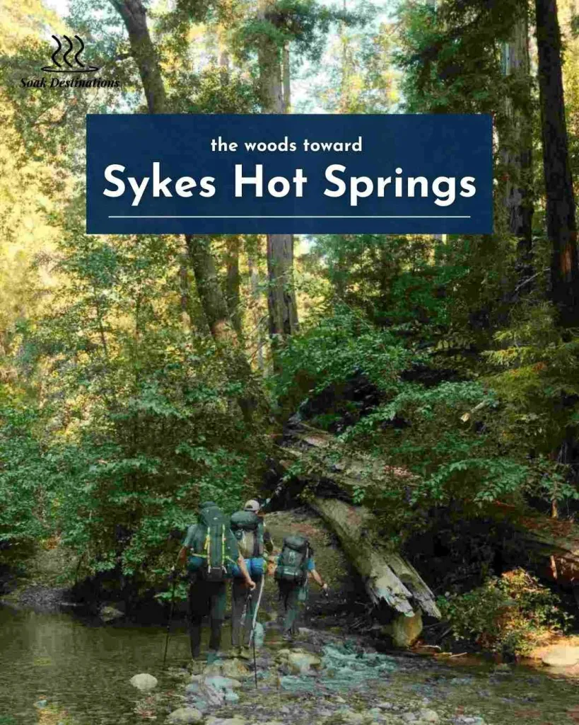 Three backpackers cross a shallow river while hiking through the woods toward Indian Hot Springs.