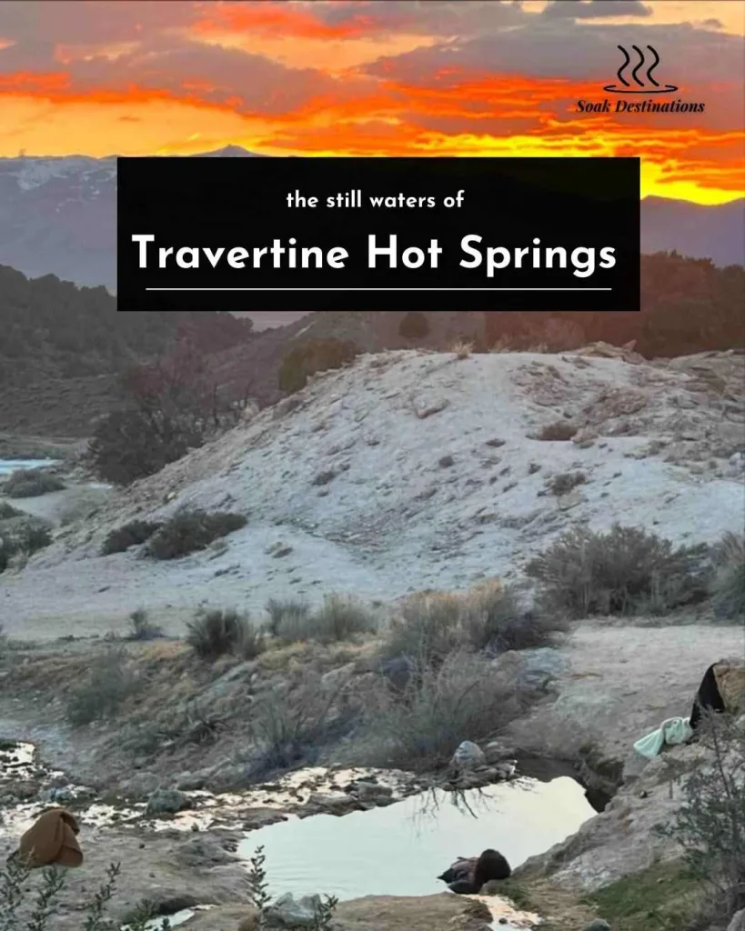A person floats in the still waters of Travertine Hot Springs during a vibrant orange sunset.