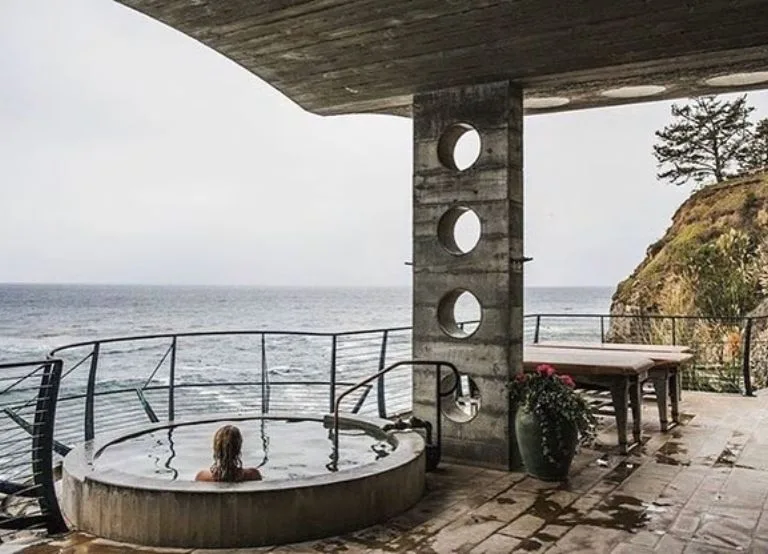 
Woman relaxing in cliffside soaking tub overlooking ocean at Esalen Hot Springs.