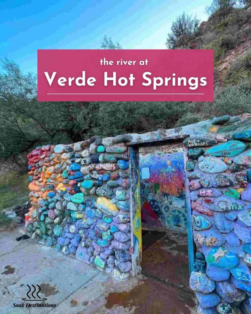 A colorful stone structure with vibrant painted rocks stands along the river at Verde Hot Springs.