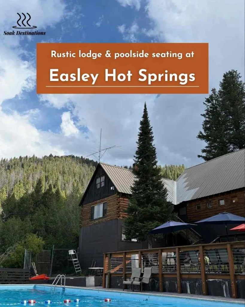 Rustic lodge and poolside seating at Easley Hot Springs nestled among pine-covered hills and open sky. 