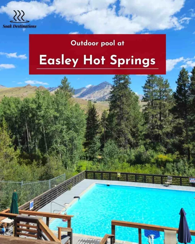 Outdoor pool at Easley Hot Springs surrounded by pine trees, green hills, and mountain peaks.